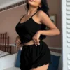 32c0dc88-7a1b-4716-a7a8-26720444cb4c Black ribbed knit cami top with crisscross back straps and matching ruffle-hem shorts pajama set styled on a bed.
