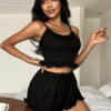 81fc6637-f872-45cb-b393-7ee7acd14208 Black ribbed knit cami top with crisscross back straps and matching ruffle-hem shorts pajama set styled on a bed.