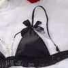 9e1dad1e-a201-4fbb-ae96-0a01e46e9668 Black satin ruffle-trim bralette and ruched thong lingerie set with delicate pearl-chain connector and bow-topped adjustable straps, styled on white backdrop with rose petals and pearls.