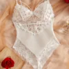 White floral lace and mesh teddy bodysuit with scalloped edges and adjustable spaghetti straps, styled on beige fabric with a red rose and vintage book page.