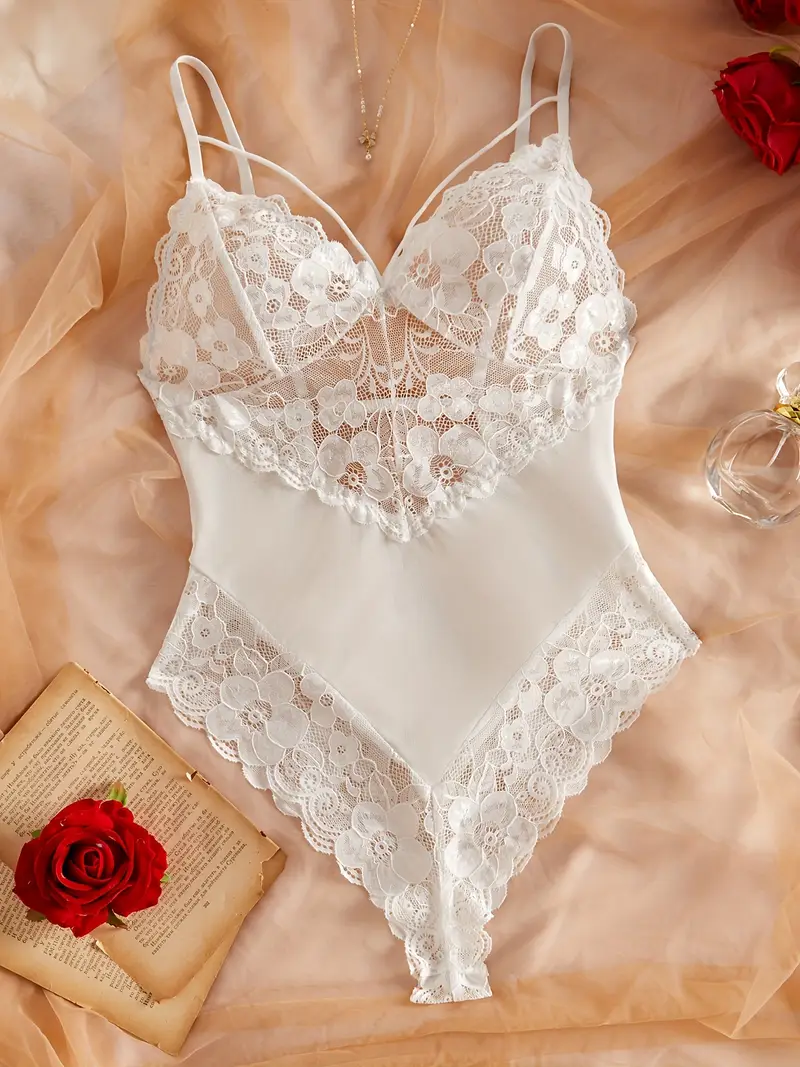 White floral lace and mesh teddy bodysuit with scalloped edges and adjustable spaghetti straps, styled on beige fabric with a red rose and vintage book page.